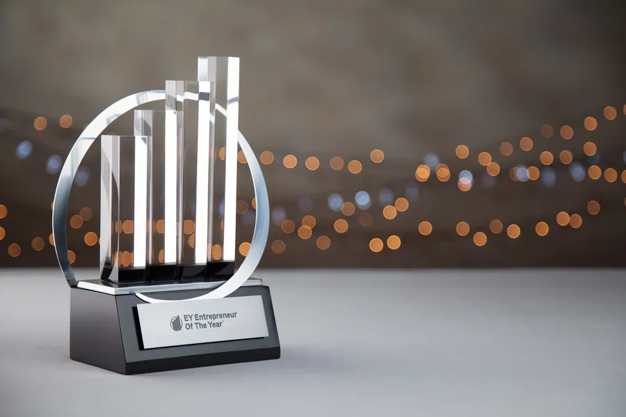 An Ernst & Young Entrepreneur of the Year crystal trophy on a black plinth, against a bokeh-lit backdrop.