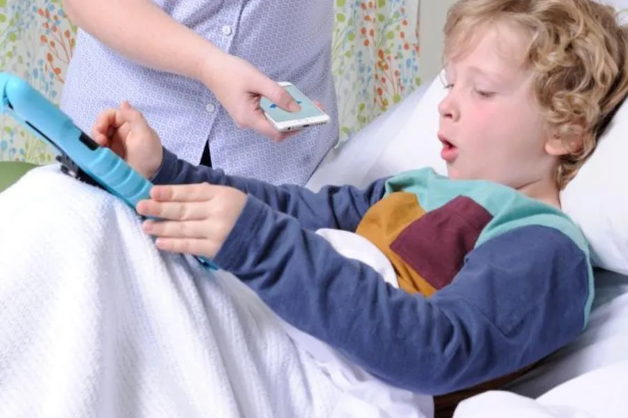 A young patient in a hospital bed coughs while a clinician records using a smartphone running ResAppDx.